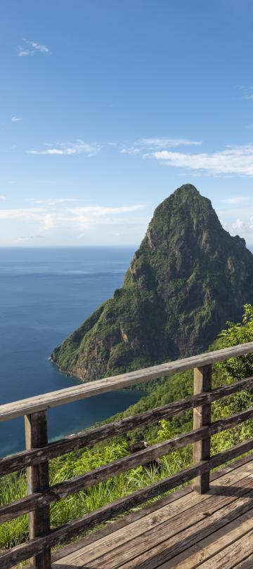 A couple looks out at the ocean and a tropical mountain from a viewing platform atop a ridge