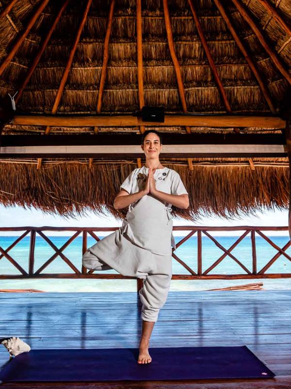 woman stands in a yoga pose thatched roof hut on beach