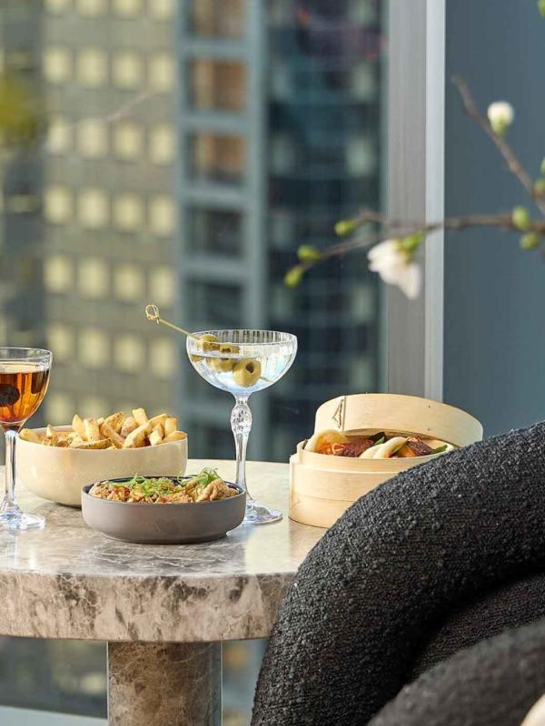 Two cocktails and snacks on a side table at Pandan, with a view of downtown Chicago