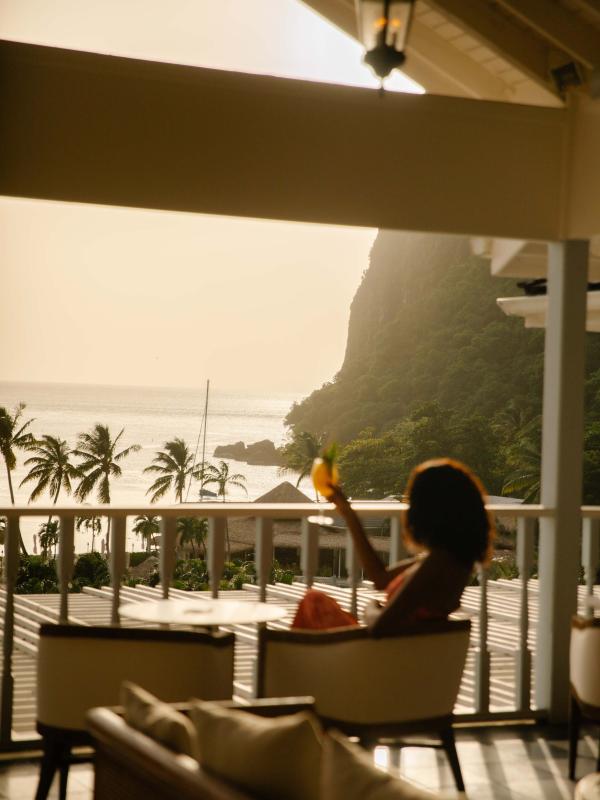A woman enjoys a drink on a shaded patio overlooking the beach