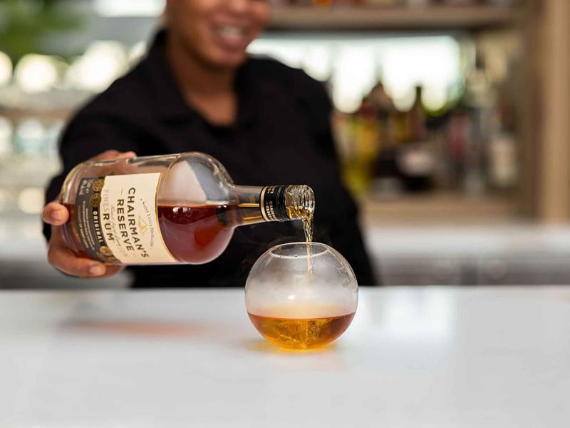 Bartender pouring rum into a spherical glass
