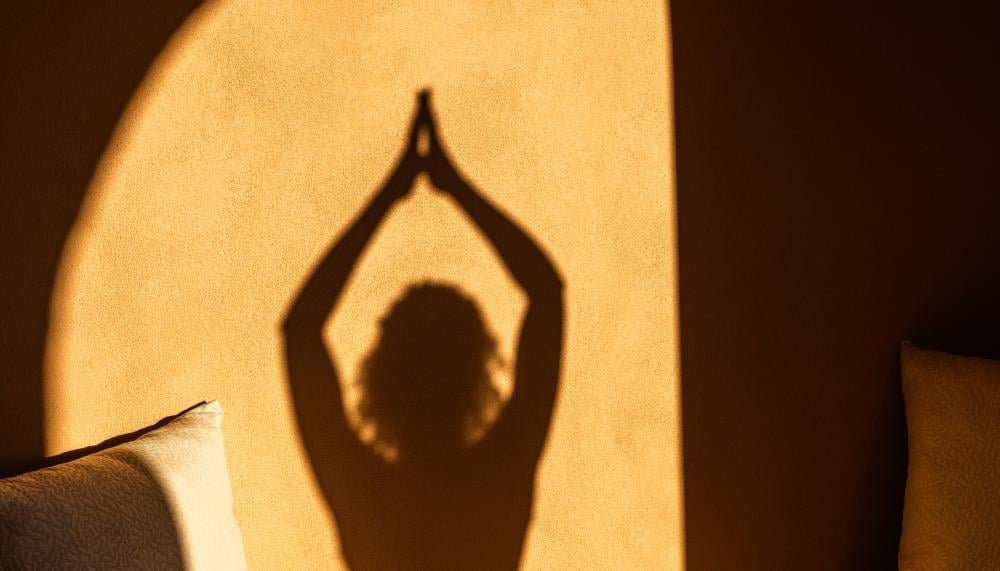 The shadow of a person doing a yoga pose on a stone wall