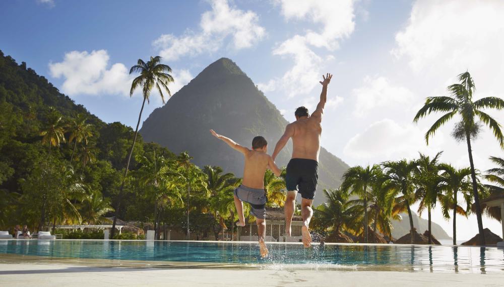 A father and son jumping into the pool at Viceroy Sugar Beach with beautiful mountains ion the foreground