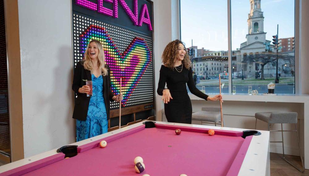 Two women shoot pool on a pink pool table at Hotel Zena's Figleaf restaurant