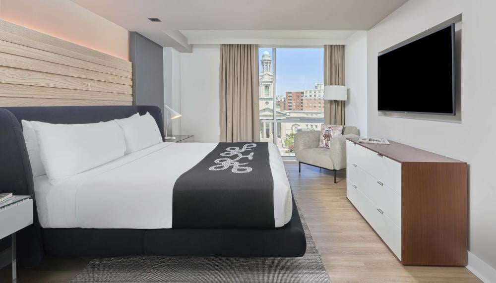 A king bed, dresser, TV, chair, and balcony in a room at Viceroy Zena Washington DC
