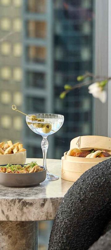 Two cocktails and snacks on a side table at Pandan, with a view of downtown Chicago
