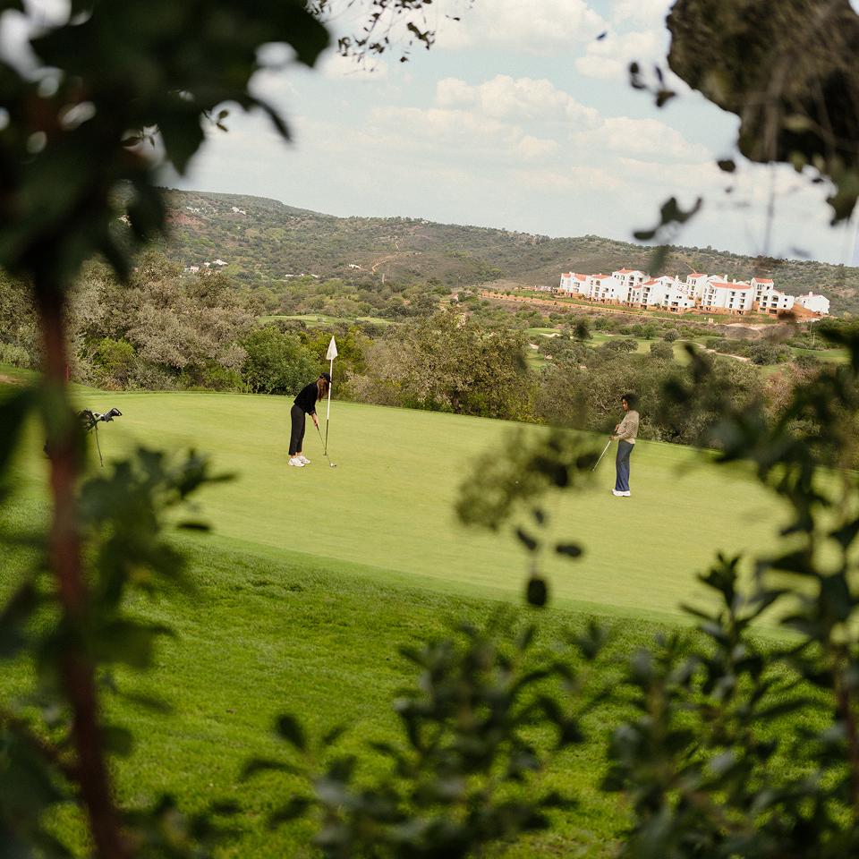 Two players on the green at Ombria golf course, with Viceroy Ombria Algarve in the background
