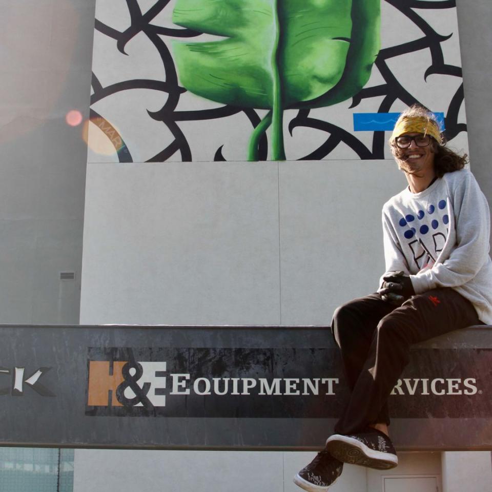 Spencer Mar Guilburt poses in front of his mural "Deep Roots"