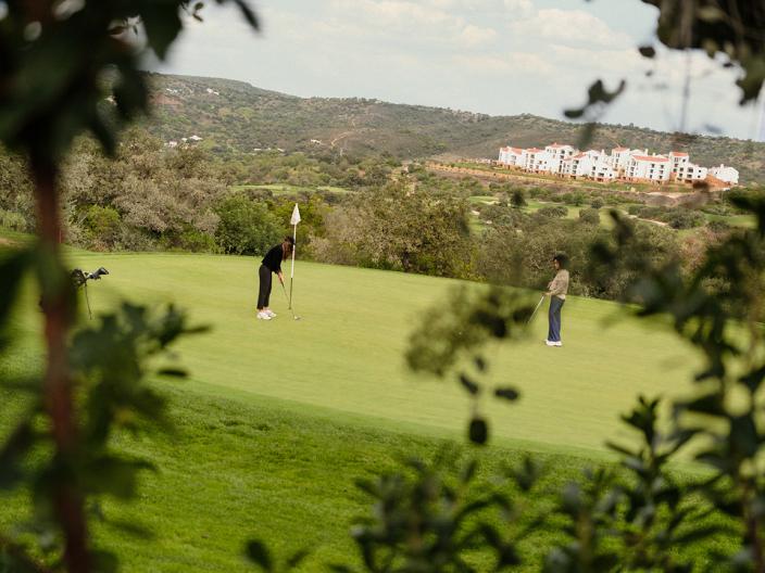 Two players on the green at Ombria golf course, with Viceroy Ombria Algarve in the background