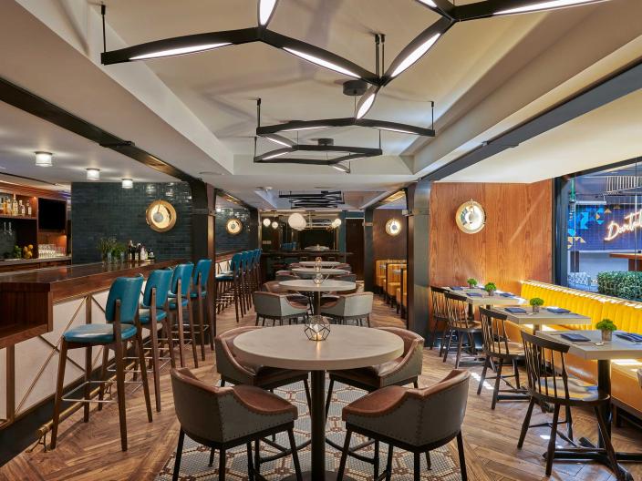 The dining room of Dovetail restaurant at Viceroy Washington DC, with yellow booths and bar seating