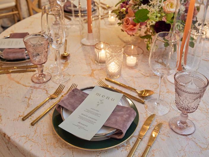An elegant place setting with gold cutlery and floral centerpieces on a white tablecloth