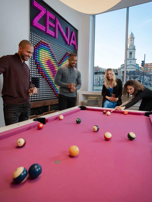 A group of people playing pool on a bright pink pooltable