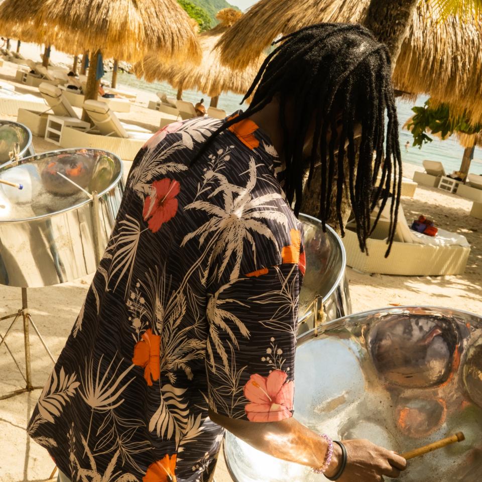 A man plays steel drums on a beach in St. Lucia, surrounded by beach huts